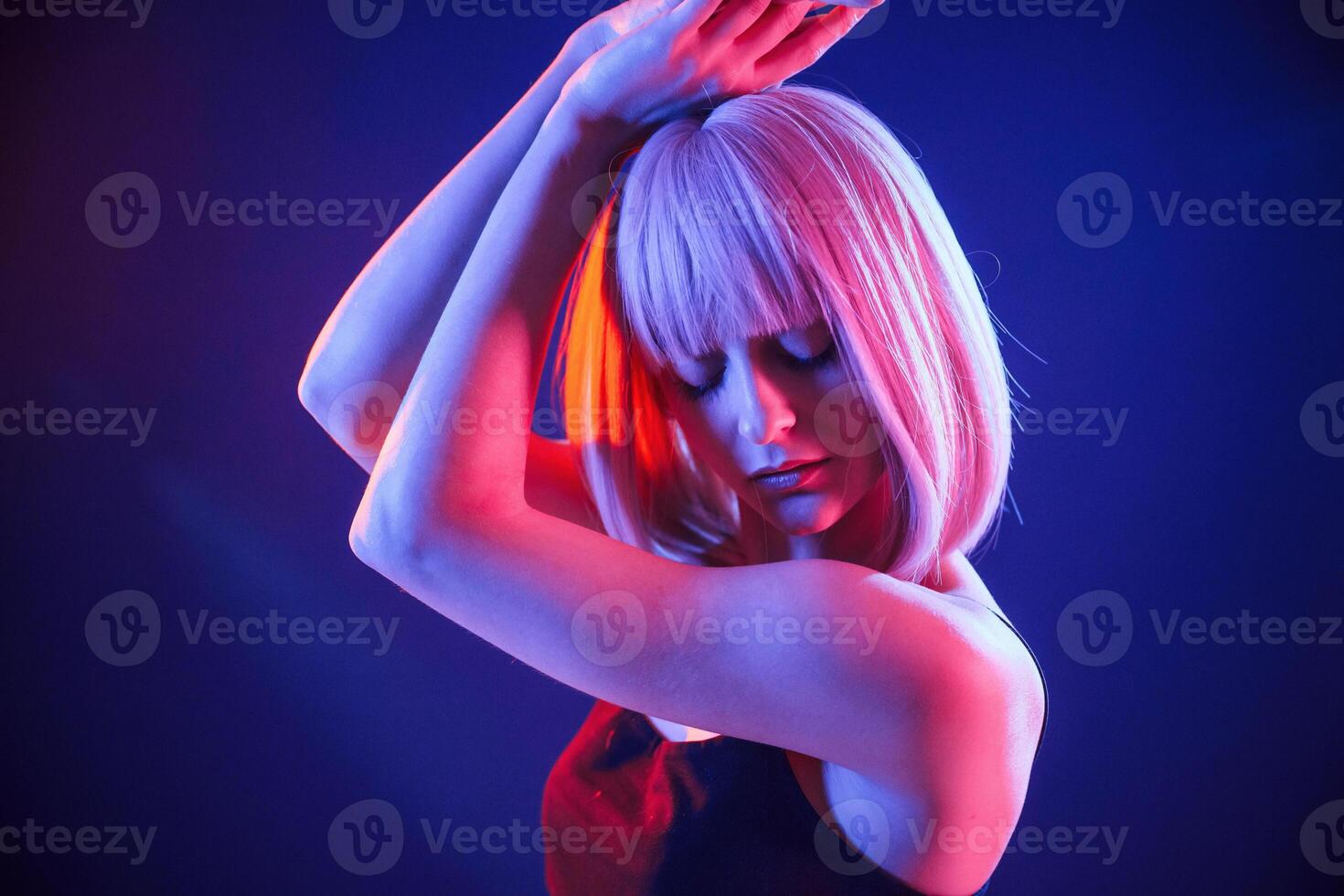 Dancing, with hands up. Woman with white hair is in studio with neon colors photo