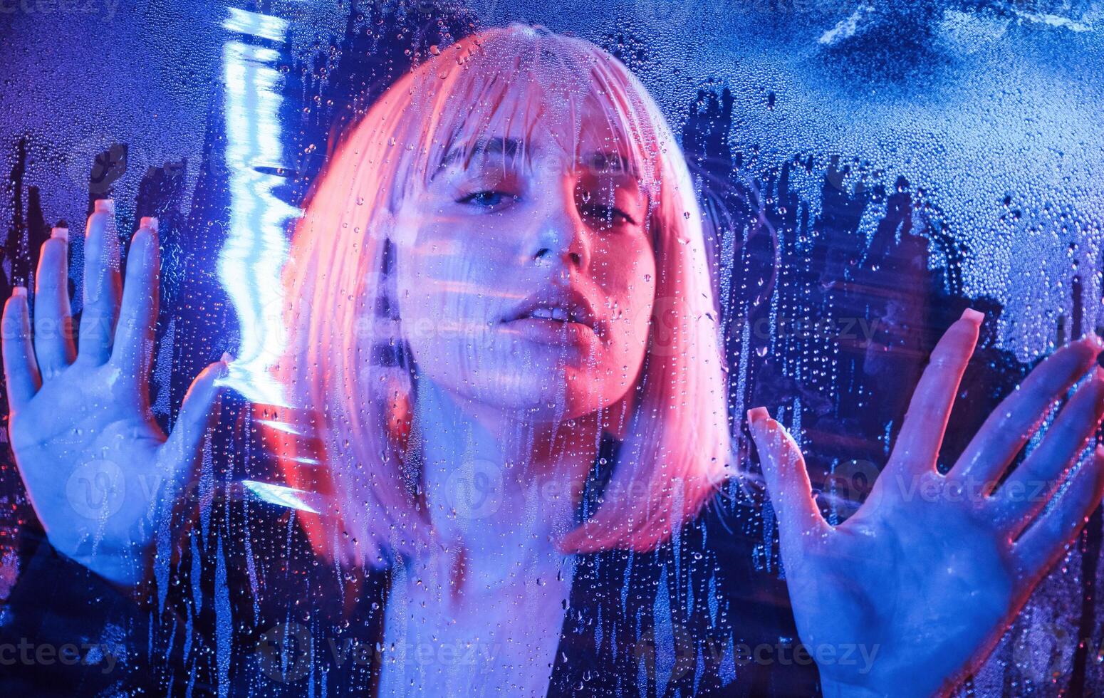Posing, calm facial expression. Stylish woman with white hair is behind wet transparent plastic sheet photo