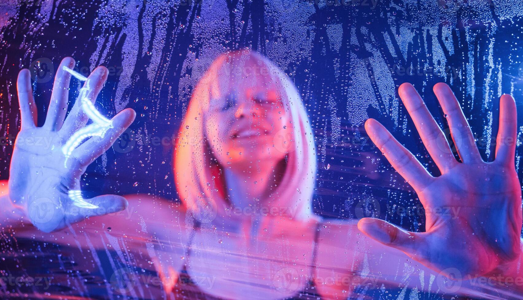 Trapped, inside, with hands on surface.. Stylish woman with white hair is behind wet transparent plastic sheet photo