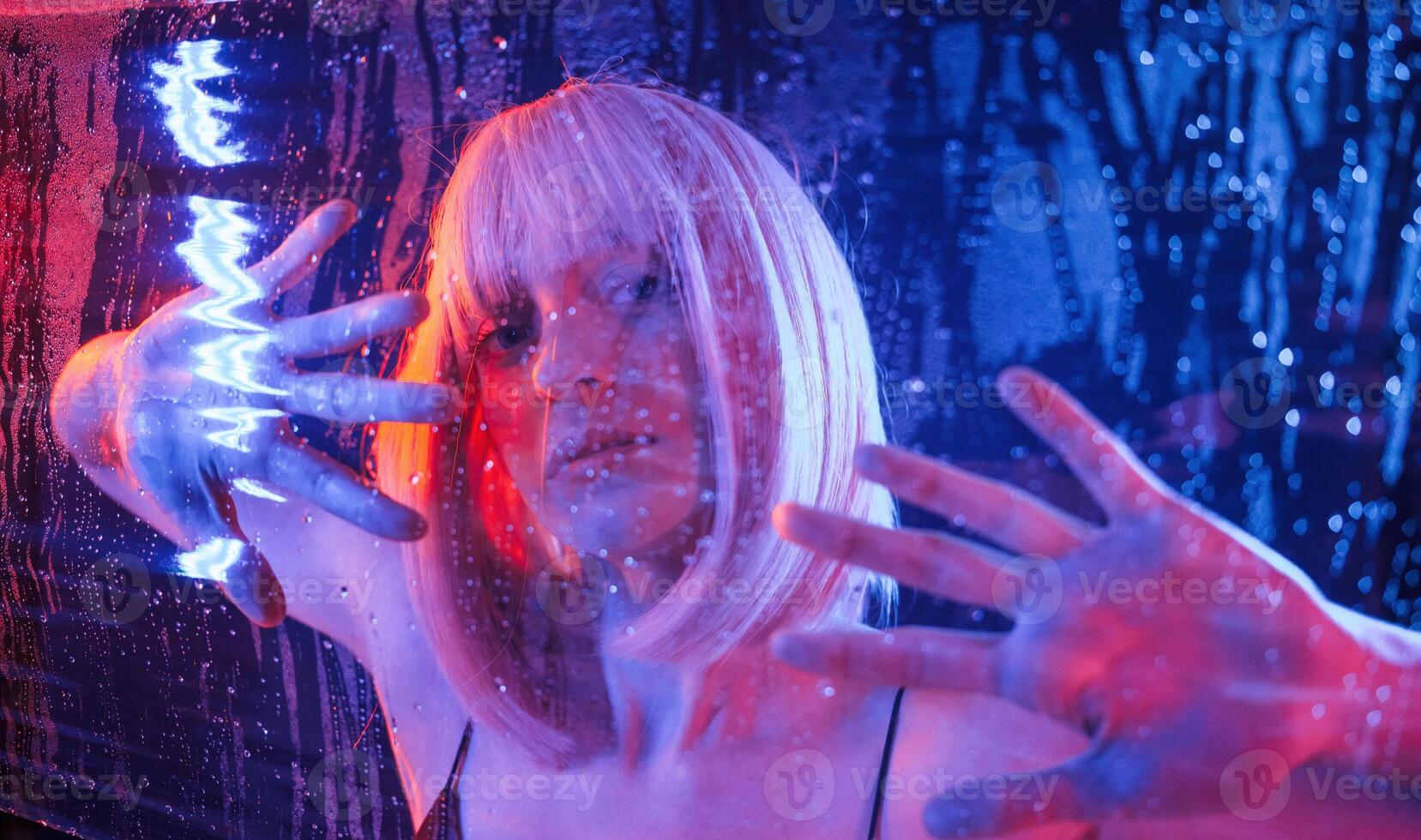 Trapped, inside, with hands,, on surface. Stylish woman with white hair is behind wet transparent plastic sheet photo