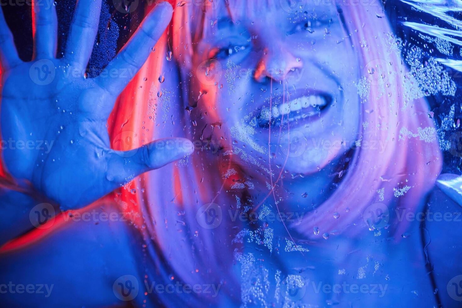Smiling, positive, facial expression. Stylish woman with white hair is behind wet transparent plastic sheet photo