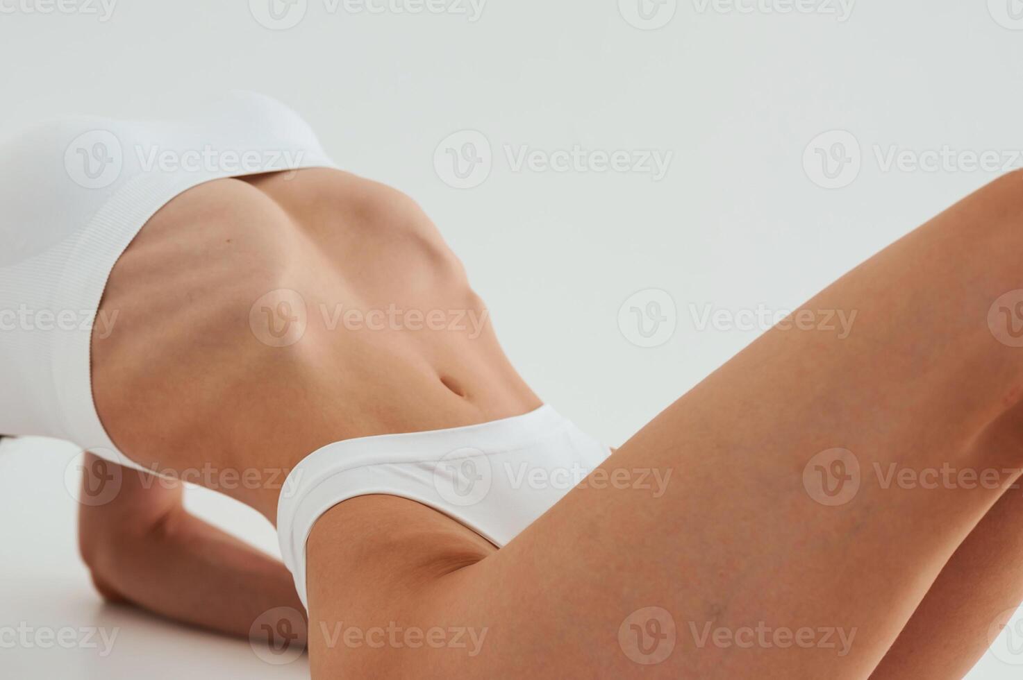 Close, up ,,view, lying down on the floor. Woman in white underwear with slim body type against white background photo