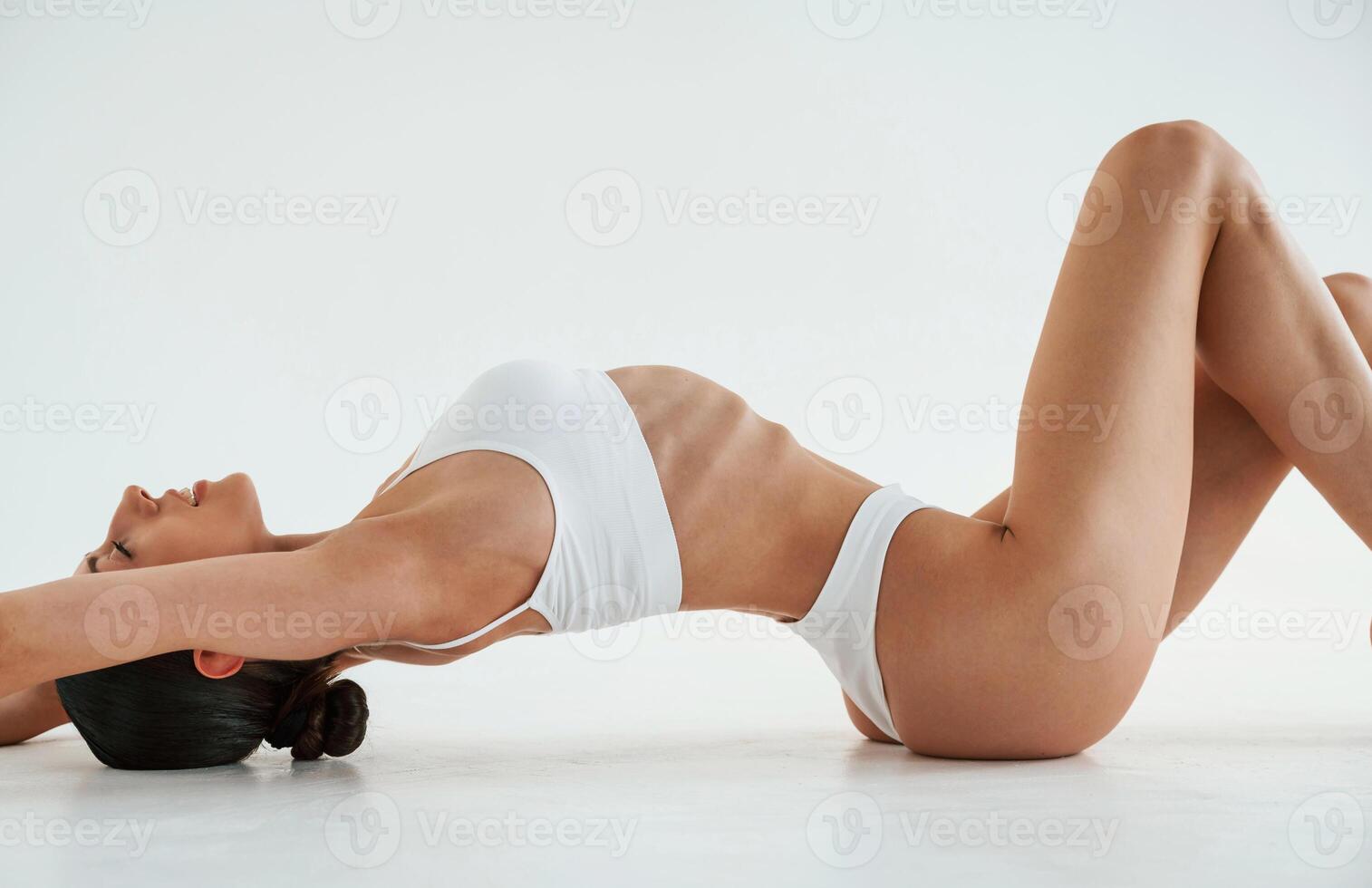 Lying ,down, on the floor. Woman in white underwear with slim body type against white background photo