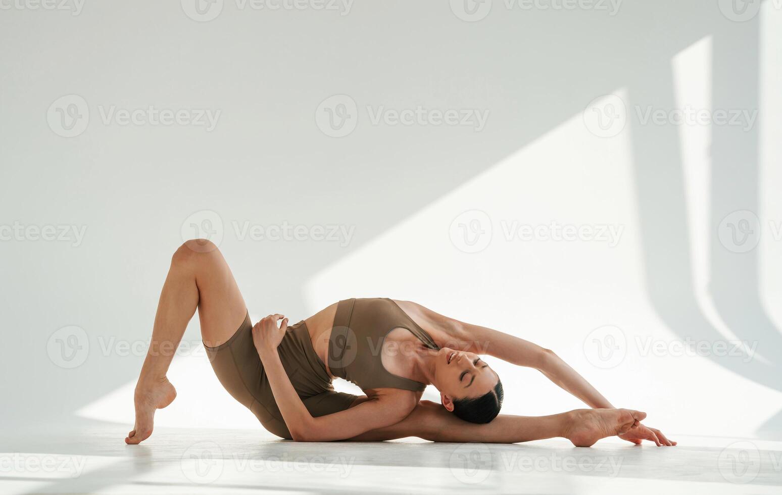 Sporty fitness exercises. Young woman is doing yoga indoors against white background photo