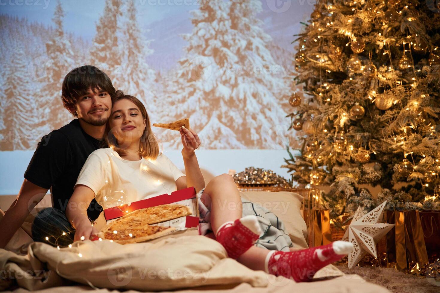 Sitting with pizza..., Beautiful young couple indoors, celebrating new year against projector photo