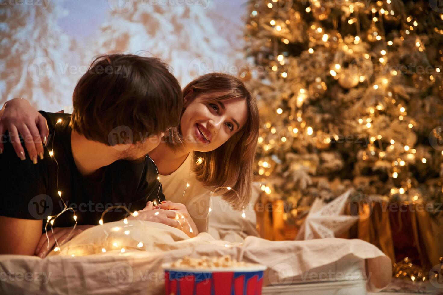 Cozy, room with, fir tree. Beautiful young couple indoors, celebrating new year against projector photo