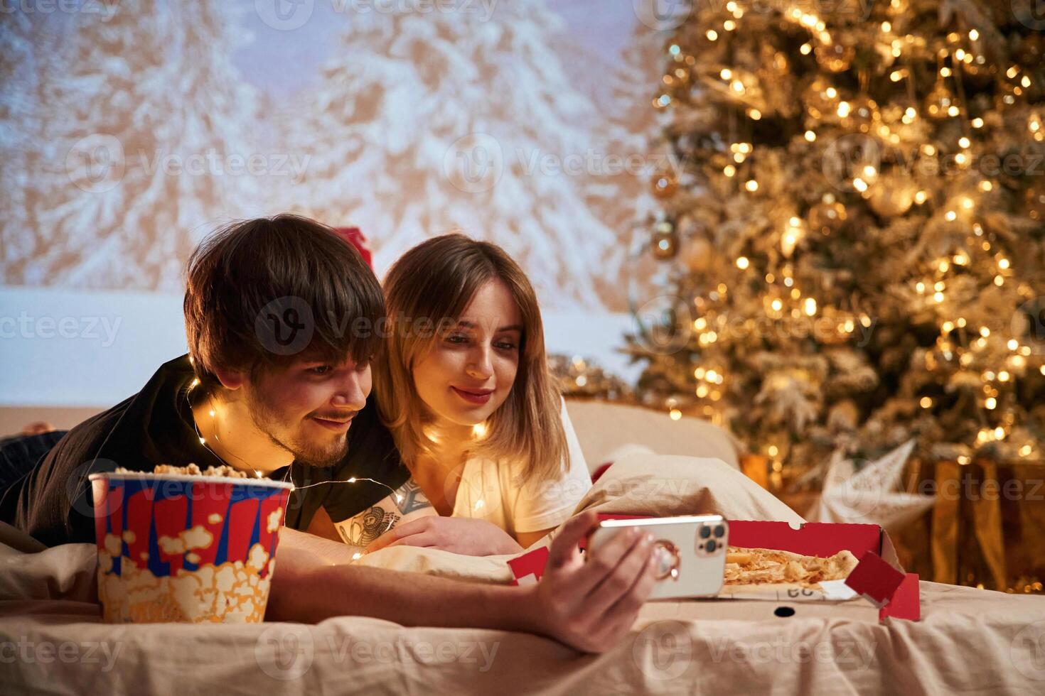 Taking,, photo by phone. Beautiful young couple indoors, celebrating new year against projector