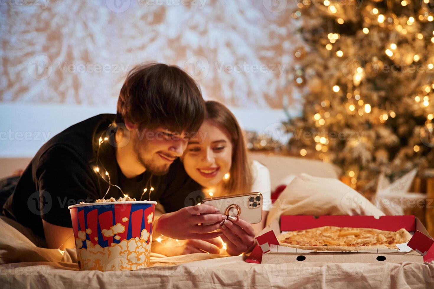 Taking, photo by phone. Beautiful young couple indoors, celebrating new year against projector