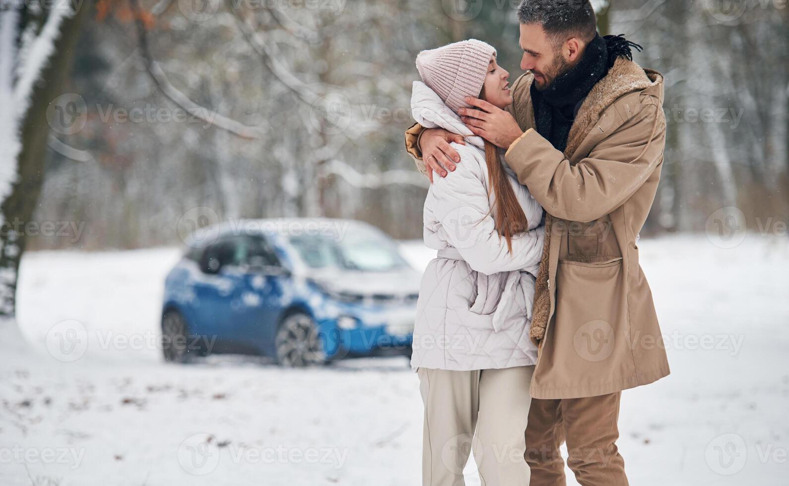 Lovely people. Happy, couple, having ,a ,walk in winter forest. Blue car is parked photo