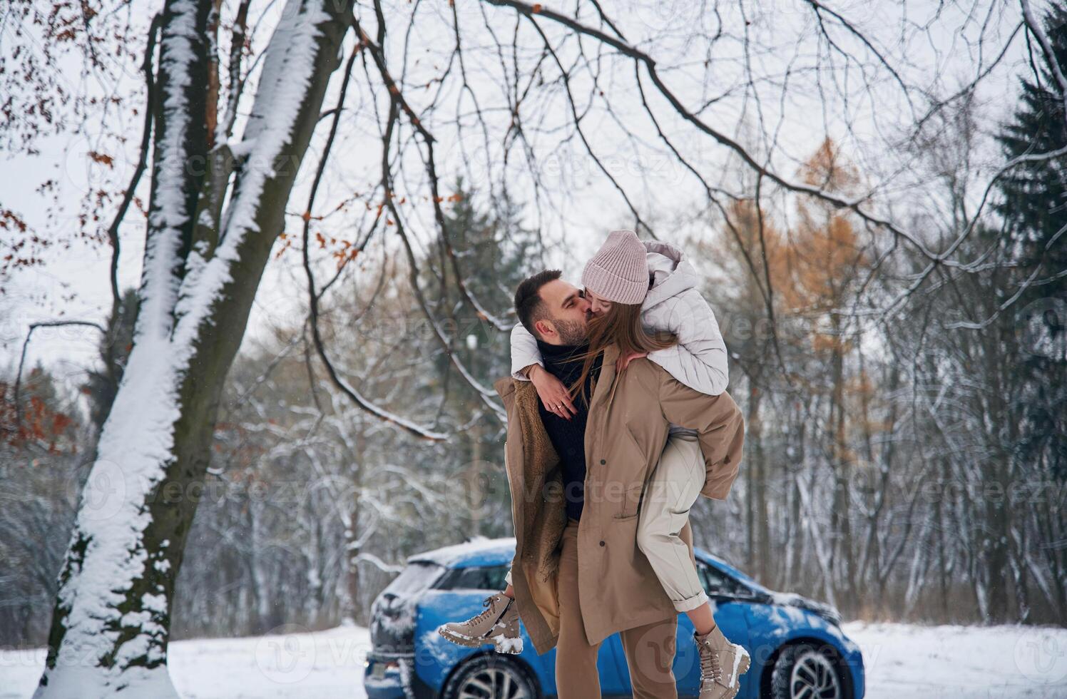 Holding ,woman... Happy couple having a walk in winter forest. Blue car is parked photo
