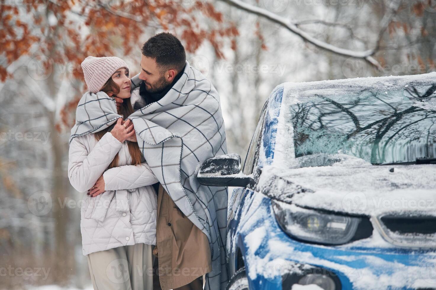 Warming by towel. Happy couple having,, a walk in winter forest. Blue car is parked photo