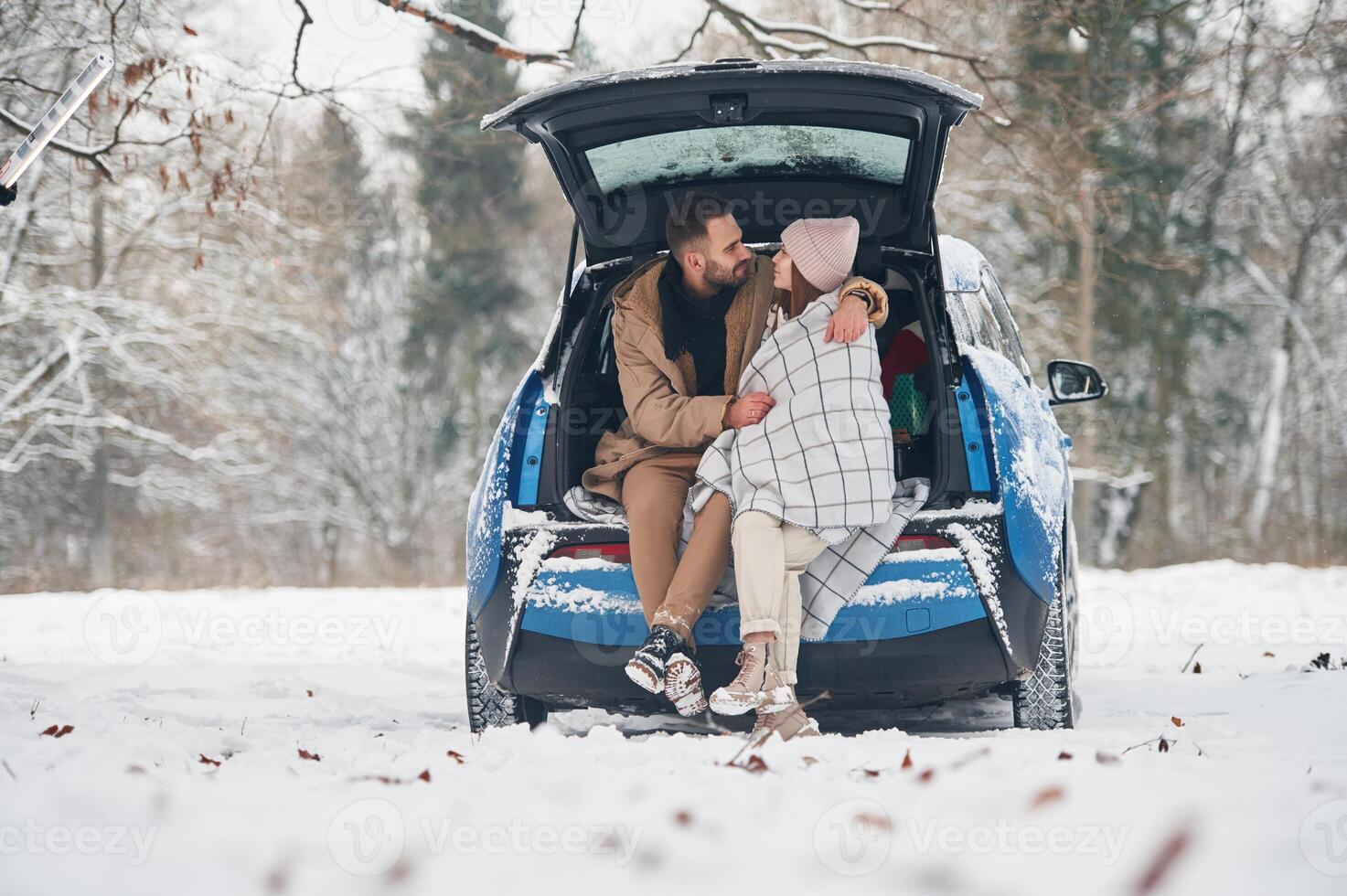 Leaning on the, automobile. Happy ,couple having a walk in winter forest. Blue car is parked photo