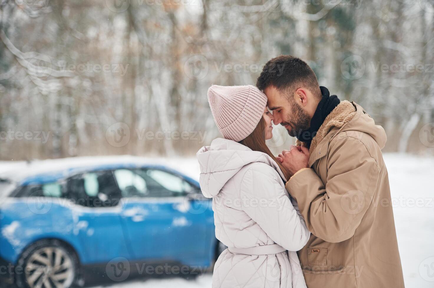 Happy couple having a walk, in winter forest. Blue car is parked photo