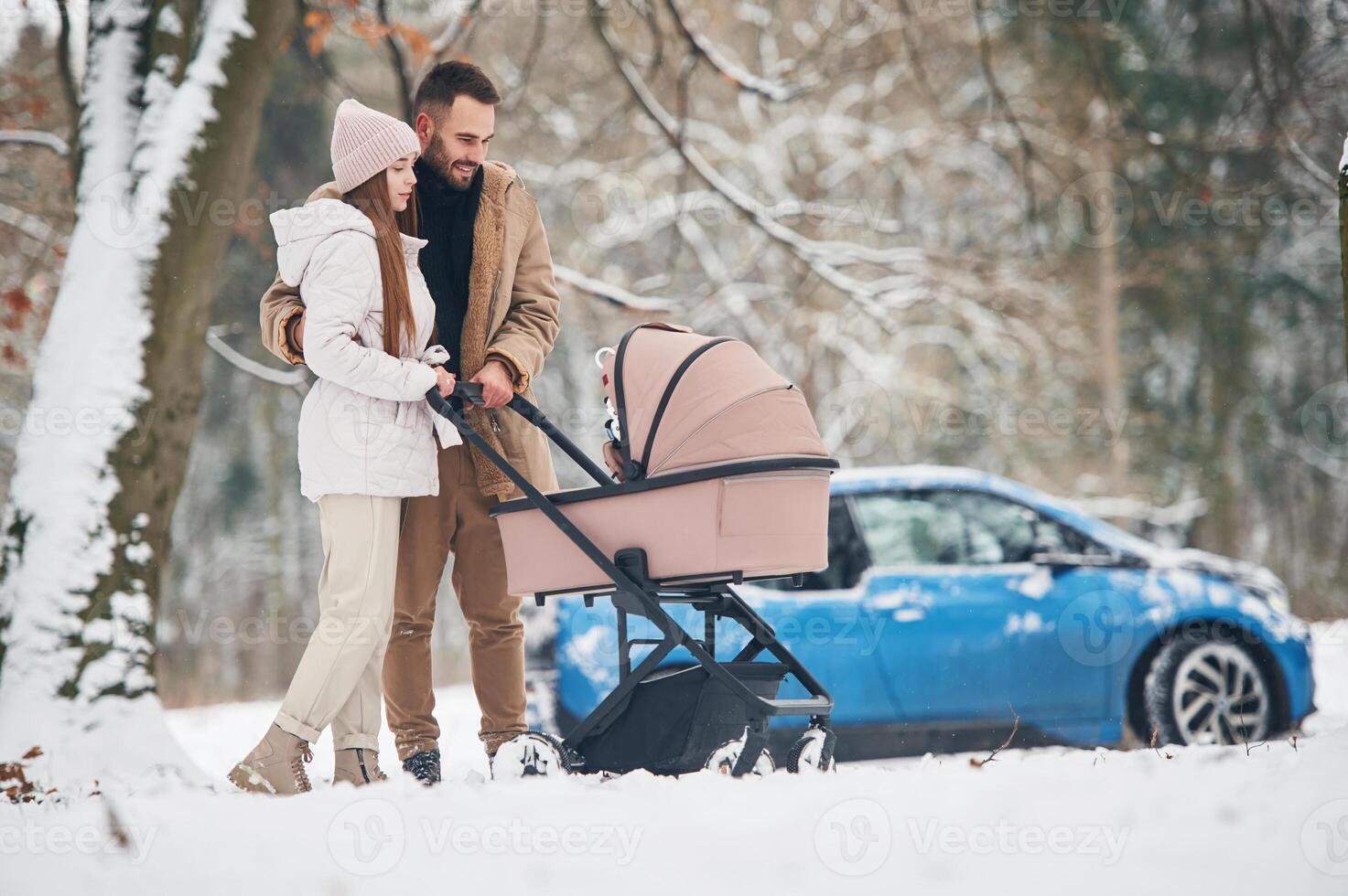 With pram. .Happy, couple having a walk in winter forest. Blue car is parked photo
