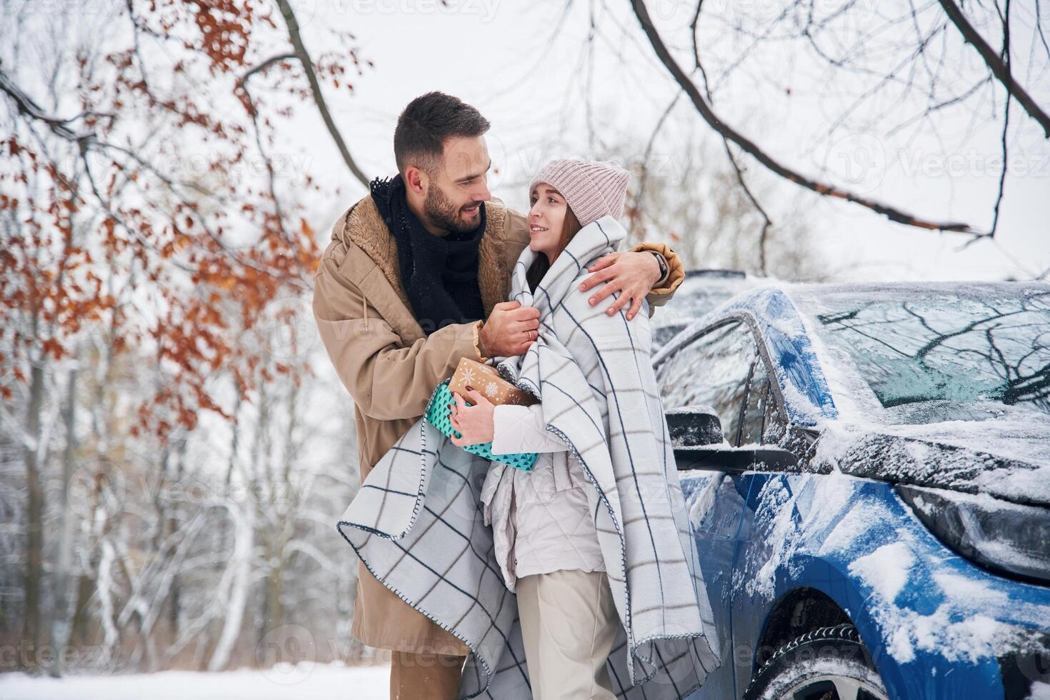 With, warm, towel. Happy couple having a walk in winter forest. Blue car is parked photo