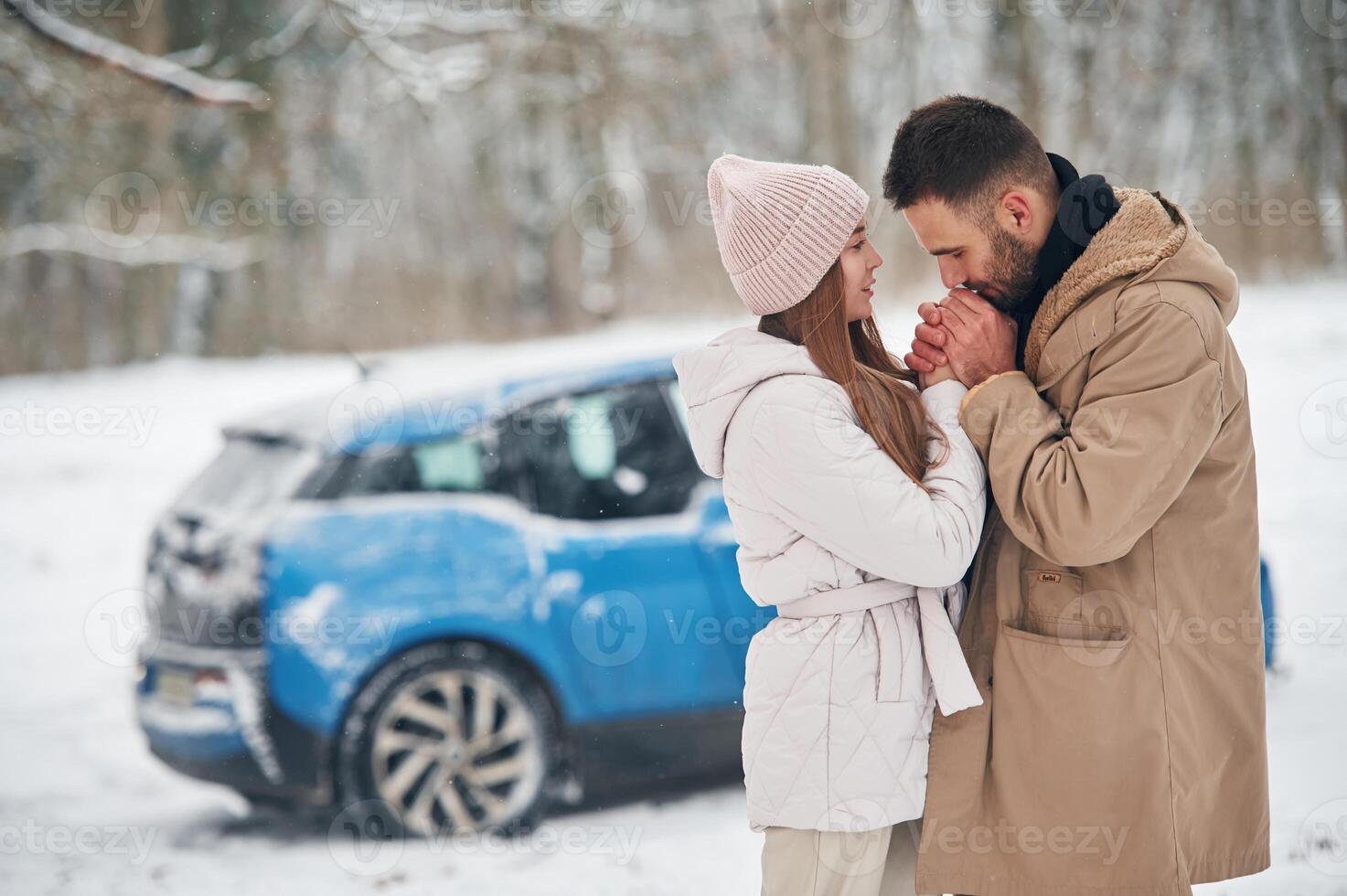 Happy ,couple having a walk in winter forest. Blue car is parked photo