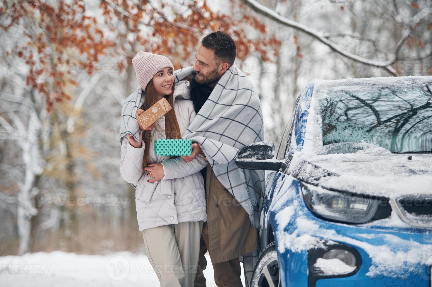 Warming by towel.. Happy couple having a walk in winter forest. Blue car is parked photo