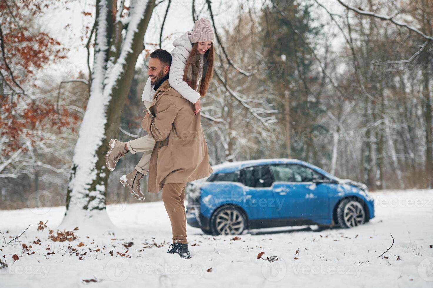 Playful ,,mood. .Happy couple having a walk in winter forest. Blue car is parked photo