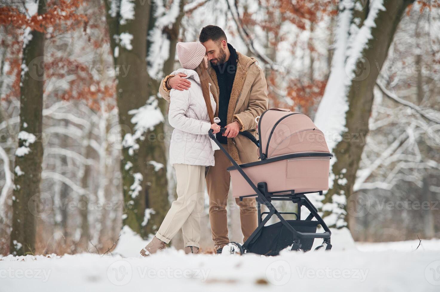 Parents, are standing with pram. Lovely couple have a walk in the winter forest photo