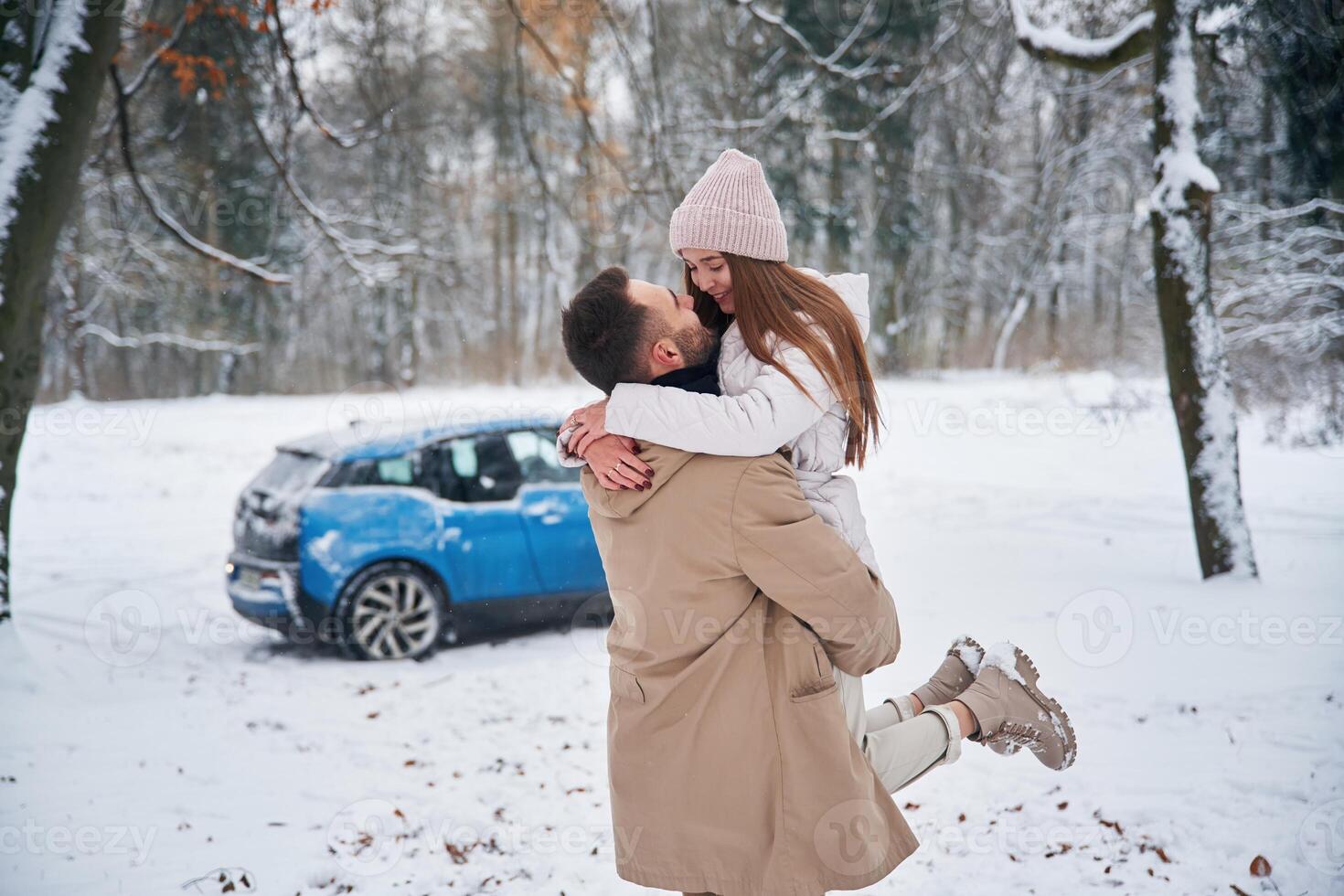 Smiling, having, fun. Happy couple having a walk in winter forest. Blue car is parked photo
