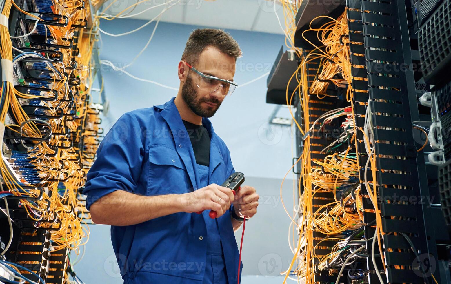 Busy by cutting the wire. Young man is working with internet equipment in server room photo