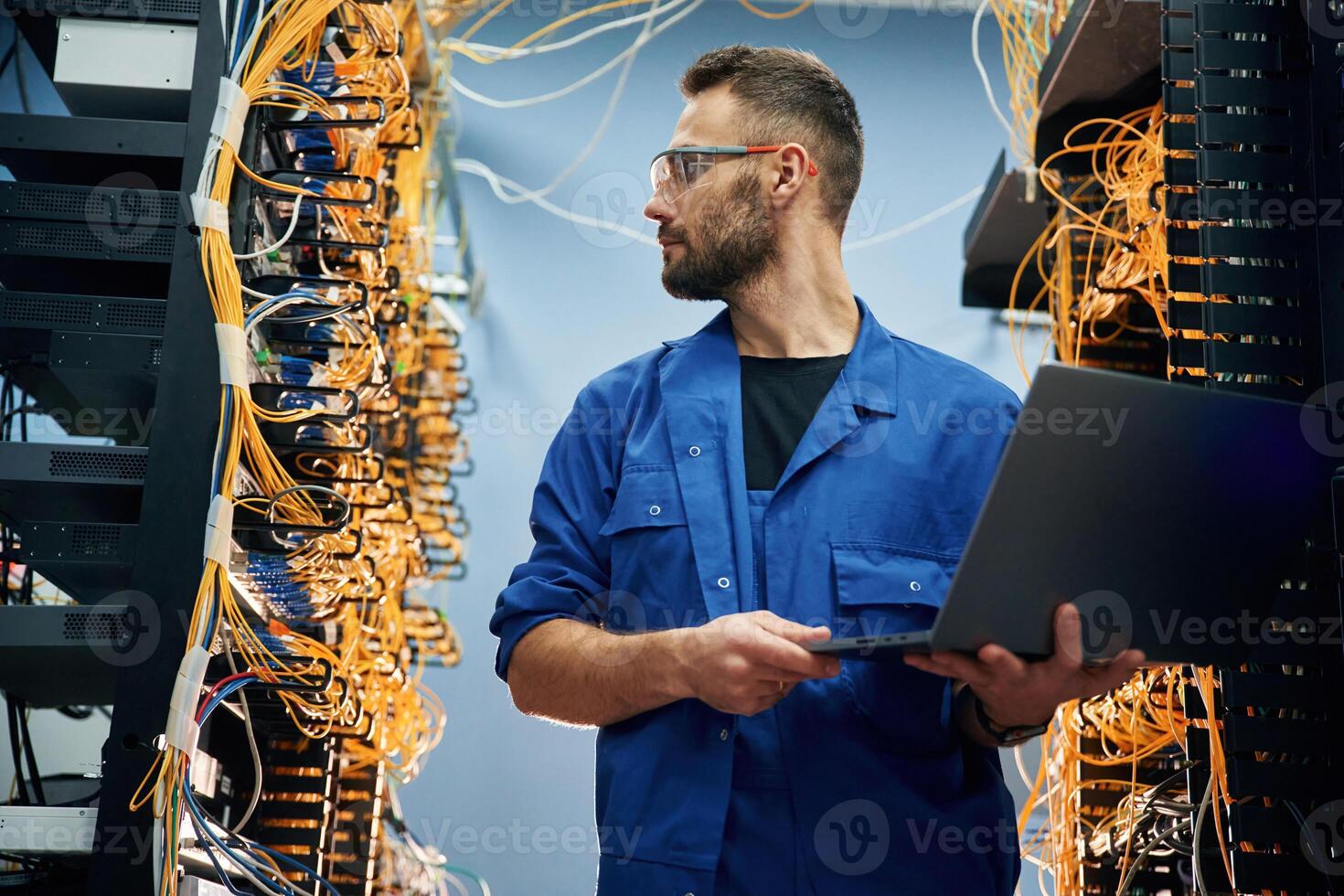 Holding laptop. Young, man, is working with internet equipment and wires in server room photo