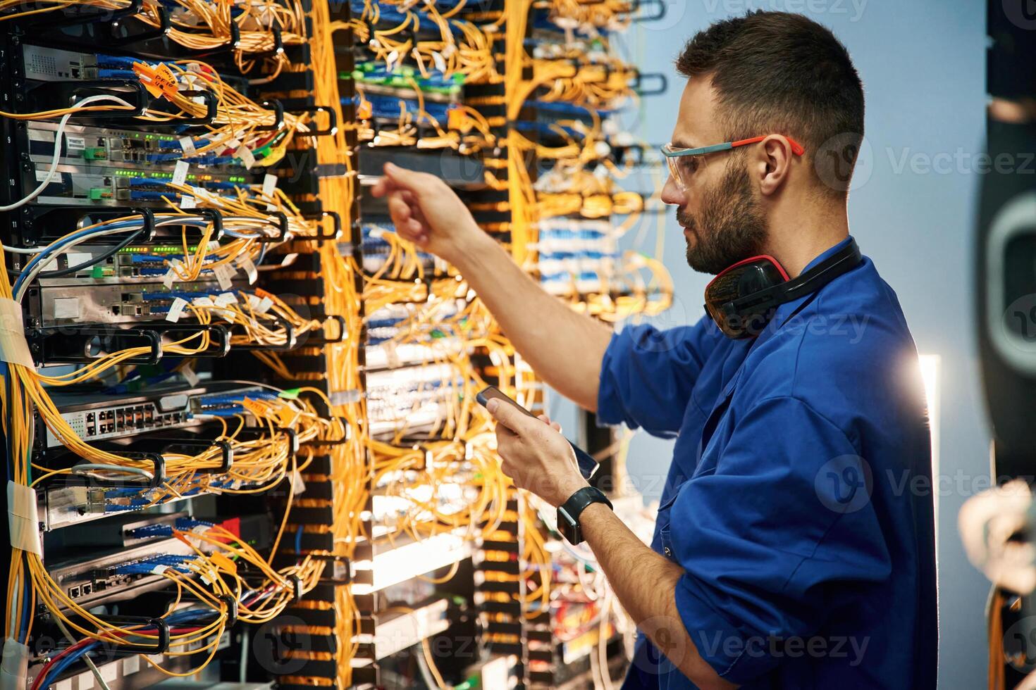 Holding smartphone.., Young man is working with internet equipment and wires in server room photo