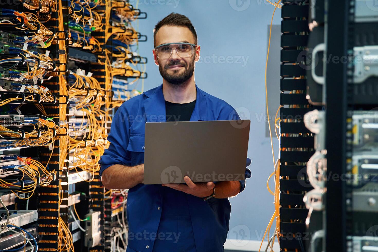 With laptop in hands. Young man is working with internet equipment and wires in server room photo