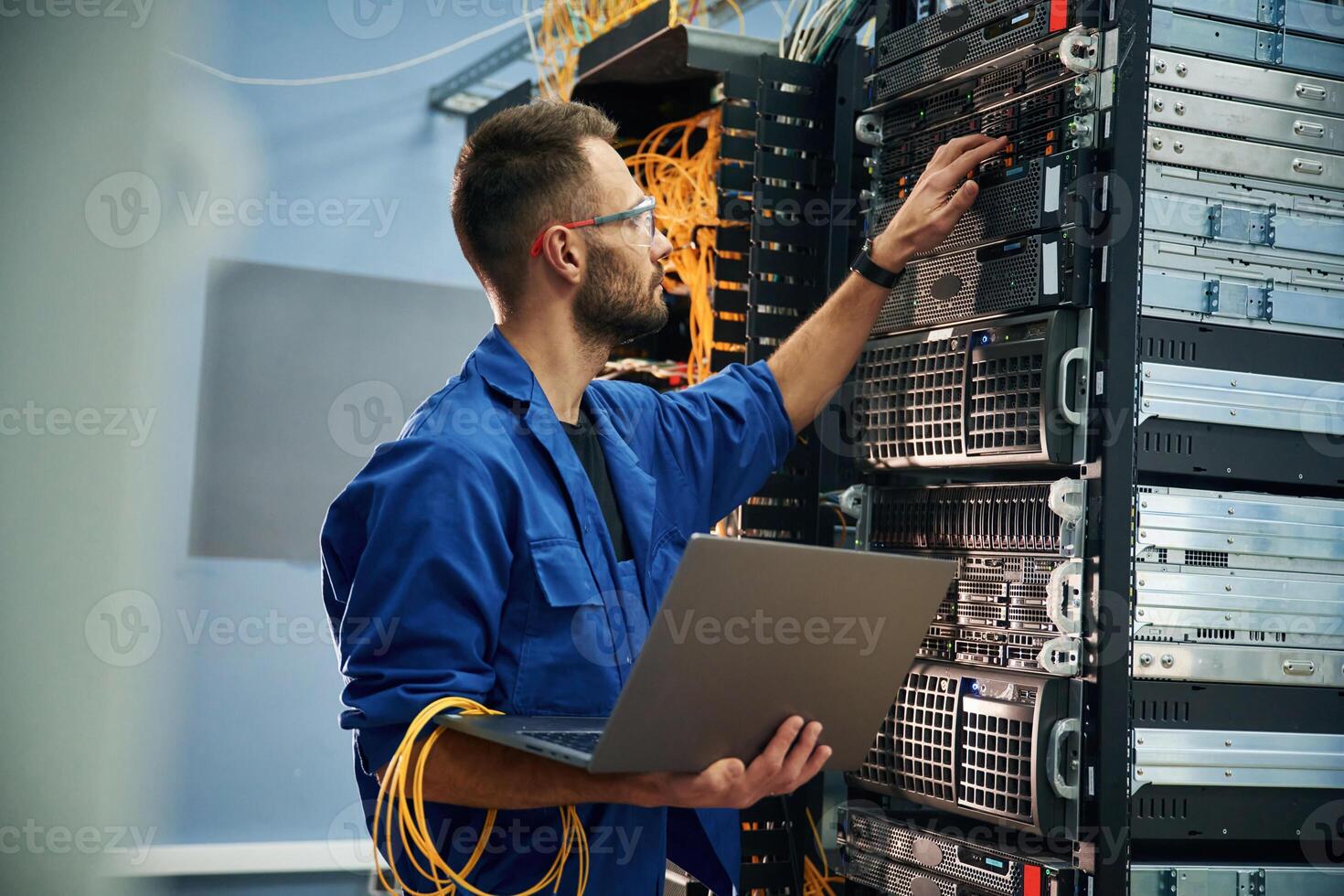 Using the laptop. Young ,man is working, with internet equipment and wires in server room photo