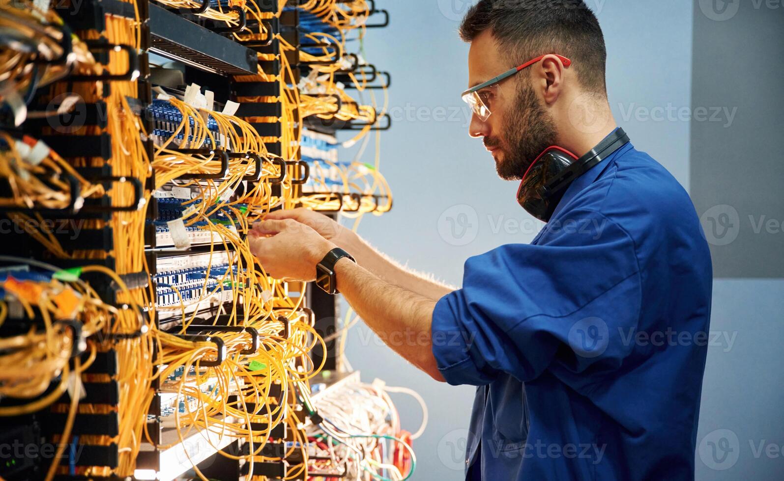 Side view. Young, man, is working with internet equipment and wires in server room photo