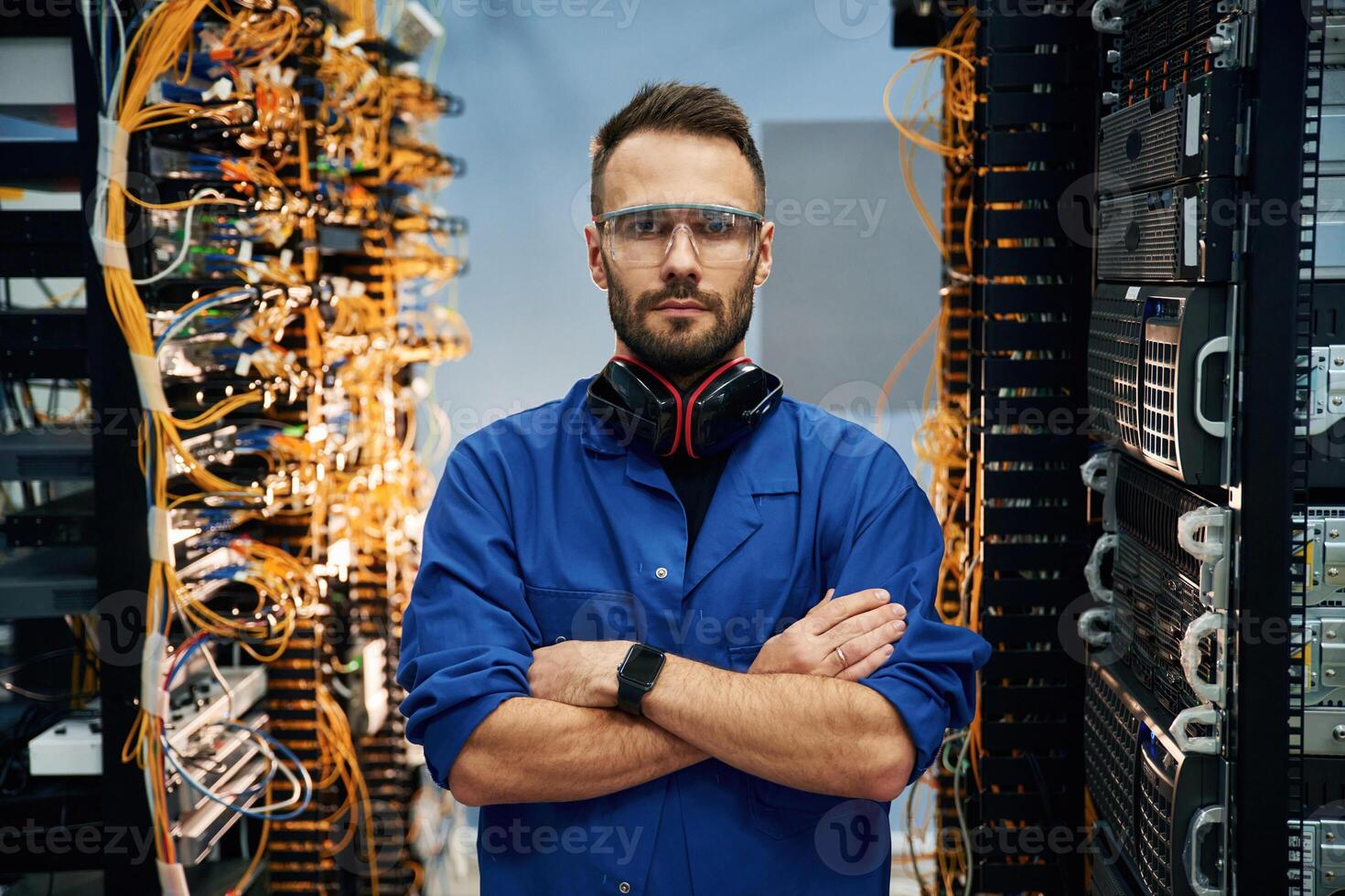 Standing with arms crossed. Young man is working with internet equipment and wires in server room photo