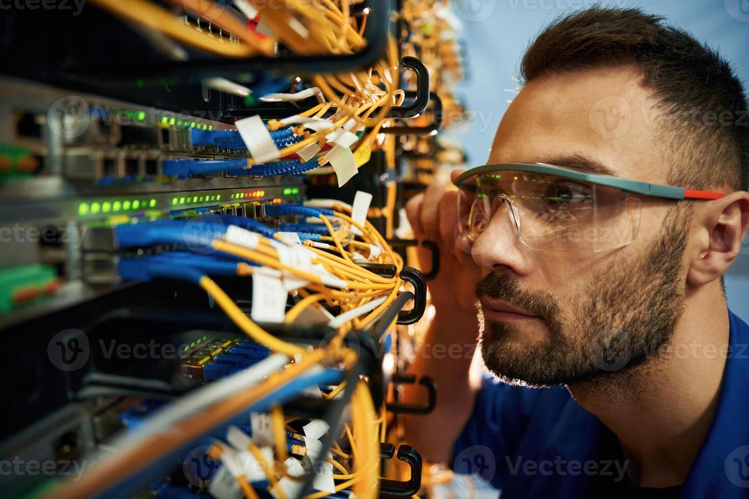 Looking extremely close, at cables. Young man is working with internet equipment and wires in server room photo