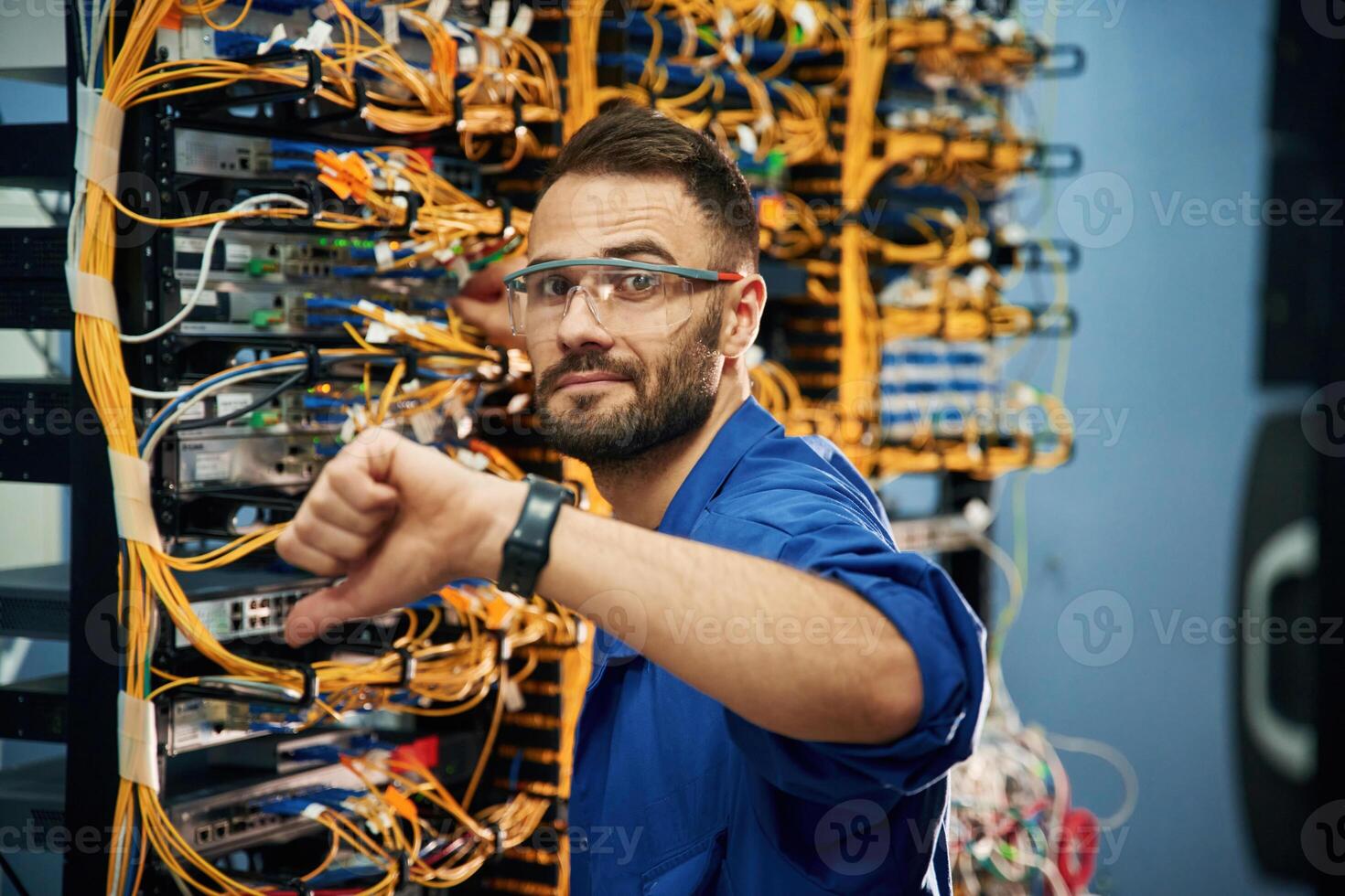 Showing, thumb down. Young man is working with internet equipment and wires in server room photo