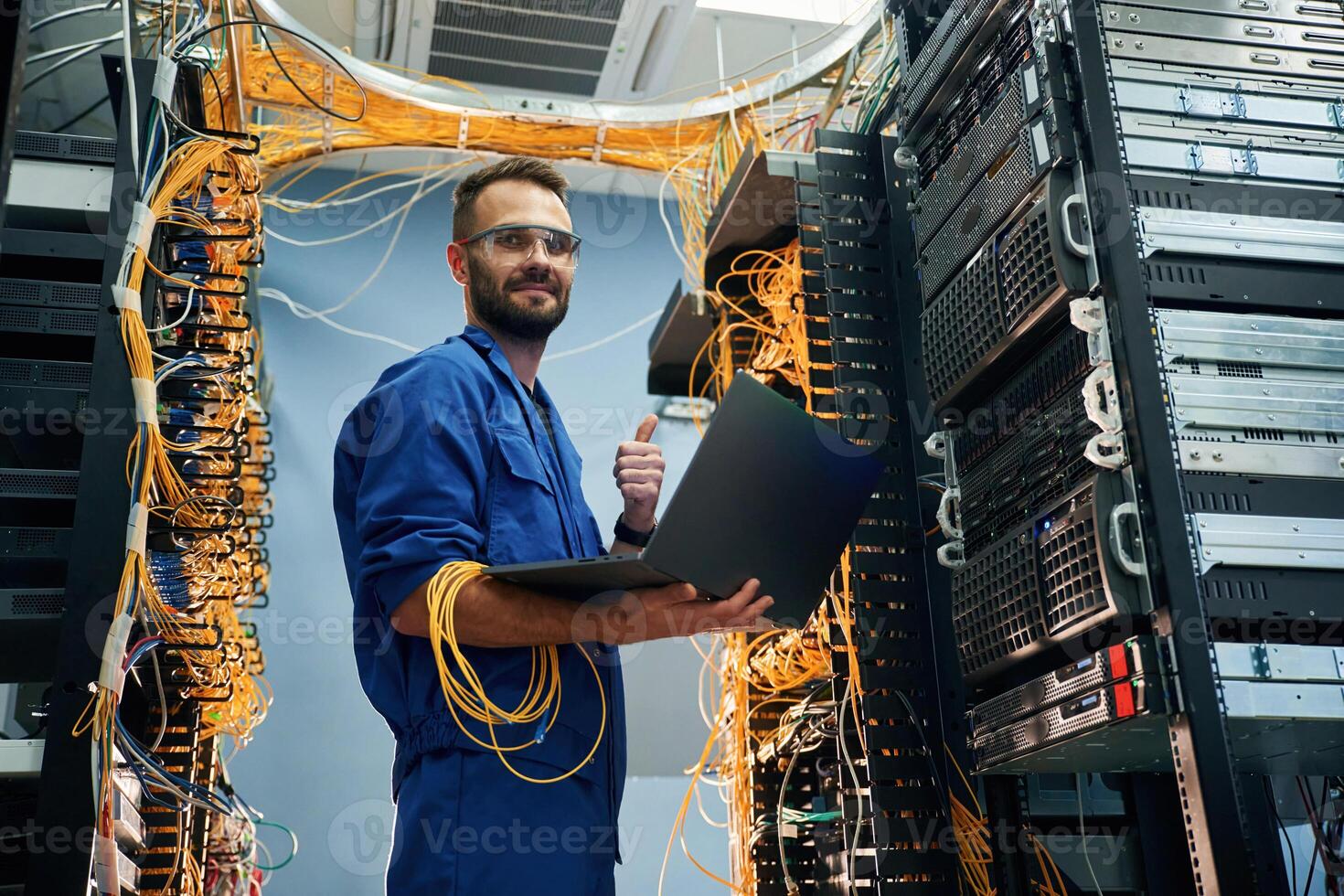 Silver colored laptop in hands.,. Young man is working with internet equipment and wires in server room photo