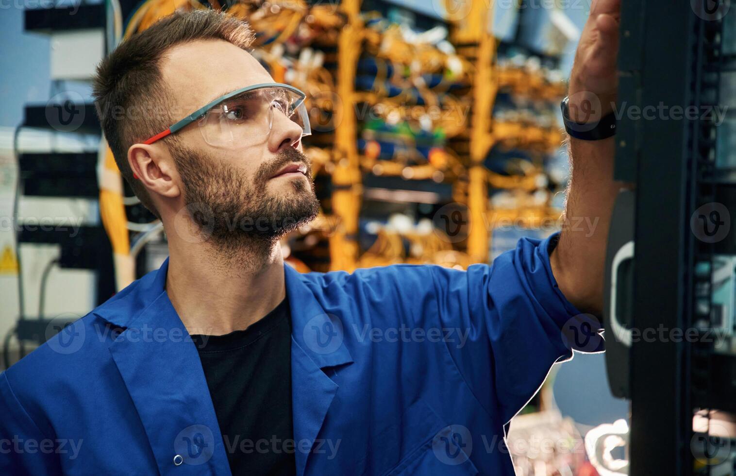 Handsome, young, man is working with internet equipment and wires in server room photo