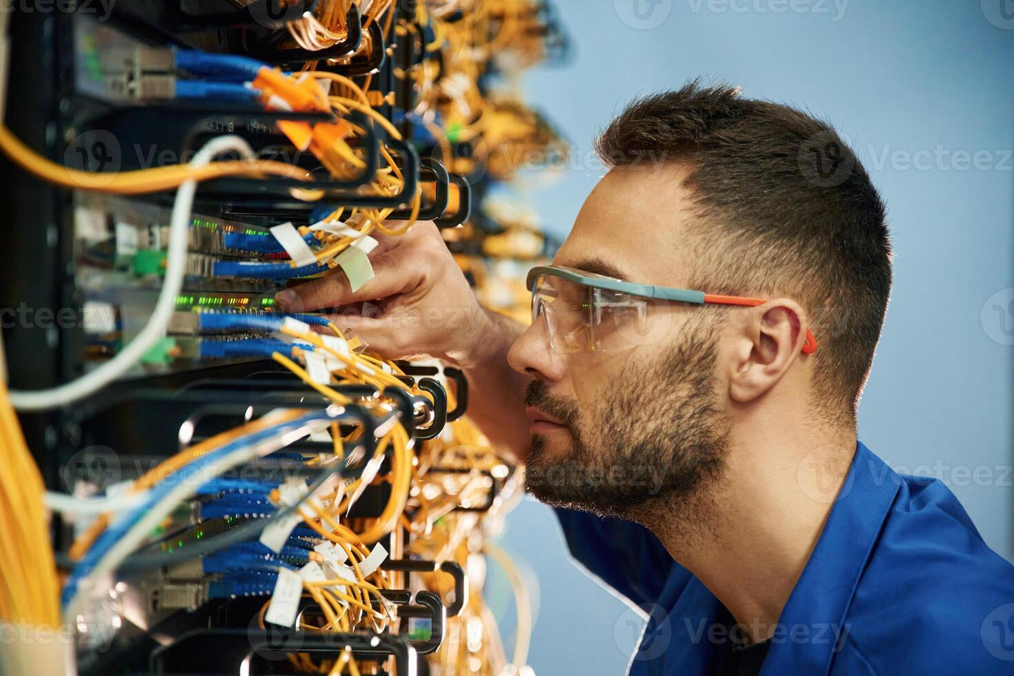Looking, extremely close at cables. Young man is working with internet equipment and wires in server room photo