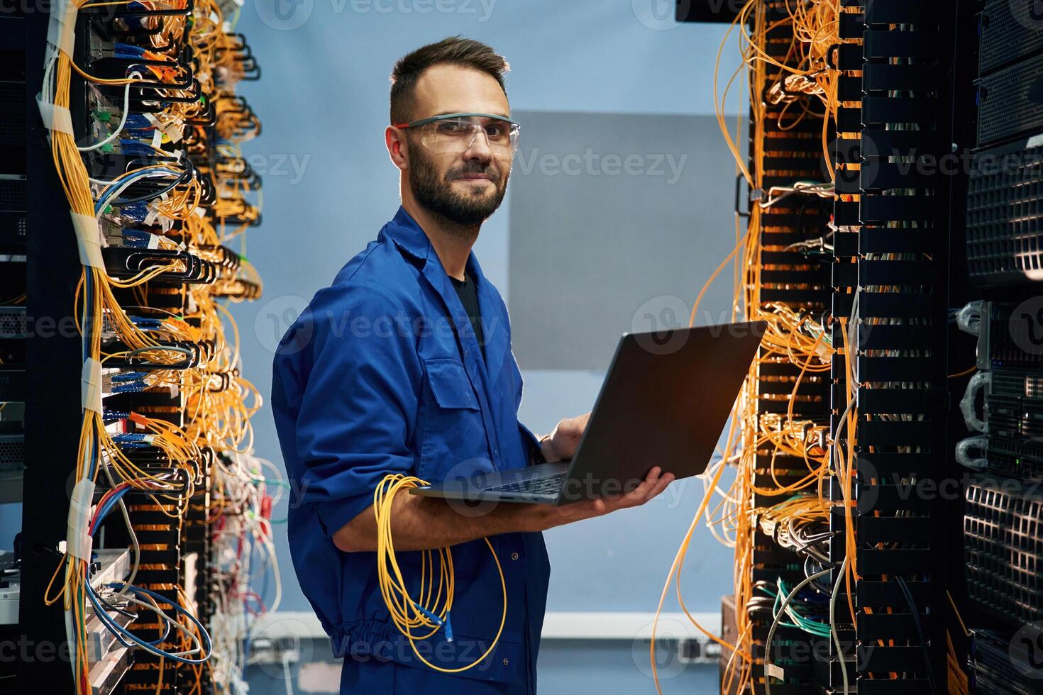 With laptop ,in hands. Young man is working with internet equipment and wires in server room photo