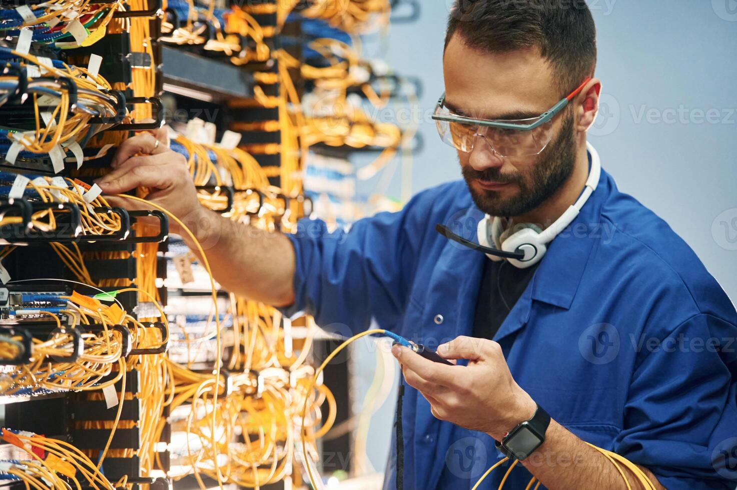 Checking, signal by ,device. Young man is working with internet equipment and wires in server room photo