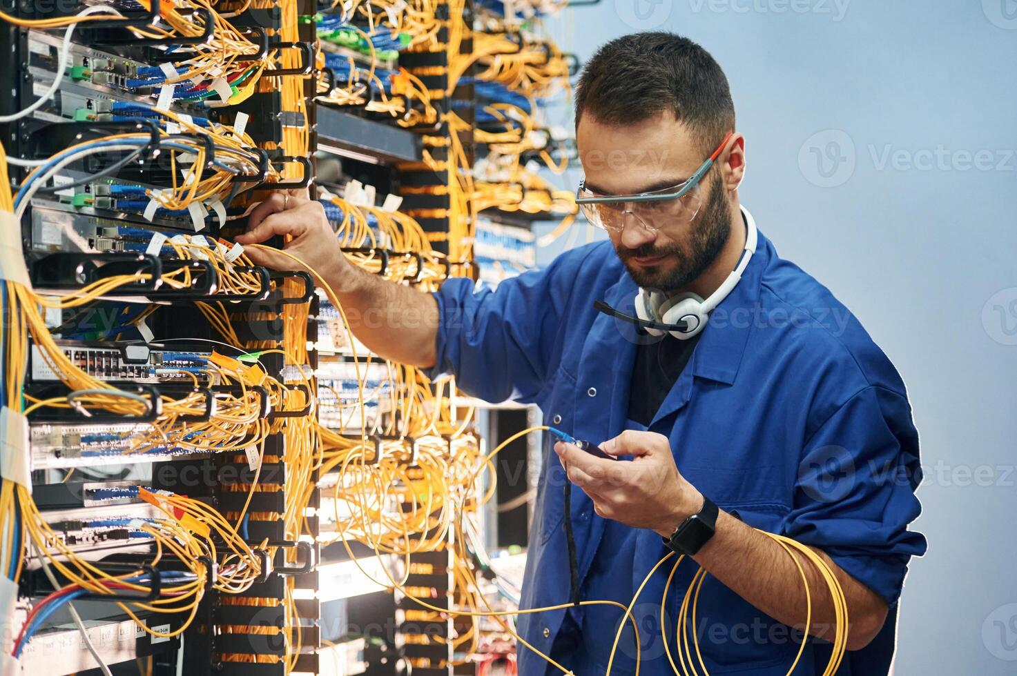Checking signal, by ,device. Young man is working with internet equipment and wires in server room photo