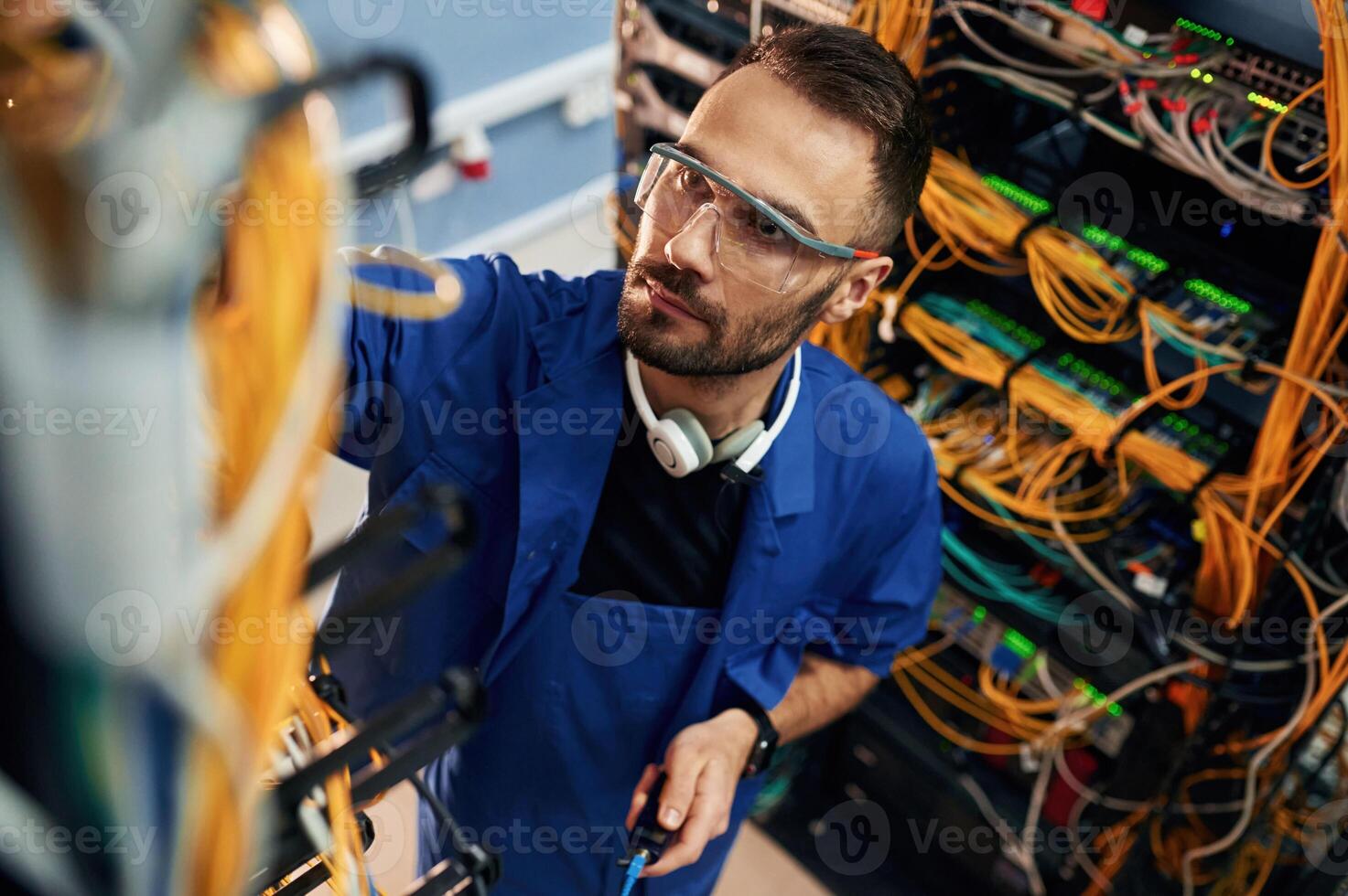 Looking, up, management, of cables. Young man is working with internet equipment and wires in server room photo