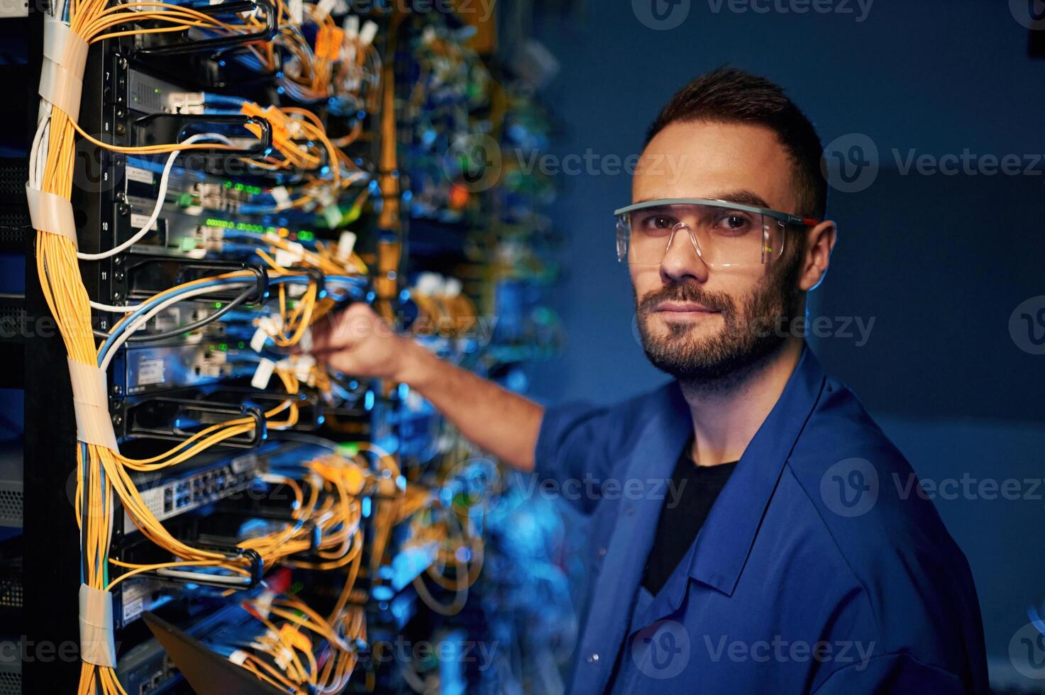 Looking to the camera... Young man is working with internet equipment and wires in server room photo
