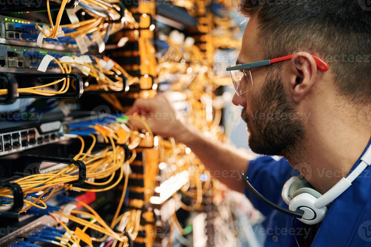 Modern, technology routing. Young man is working with internet equipment and wires in server room photo