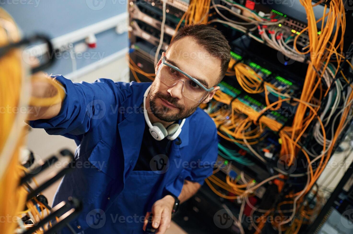 Looking up, management of cables.. Young man is working with internet equipment and wires in server room photo