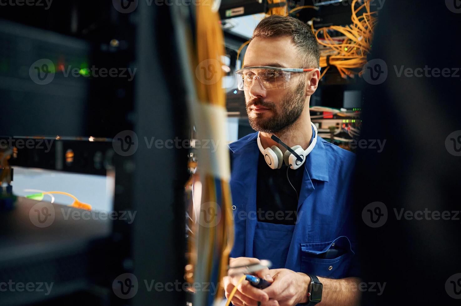 In blue,, colored uniform. Young man is working with internet equipment and wires in server room photo
