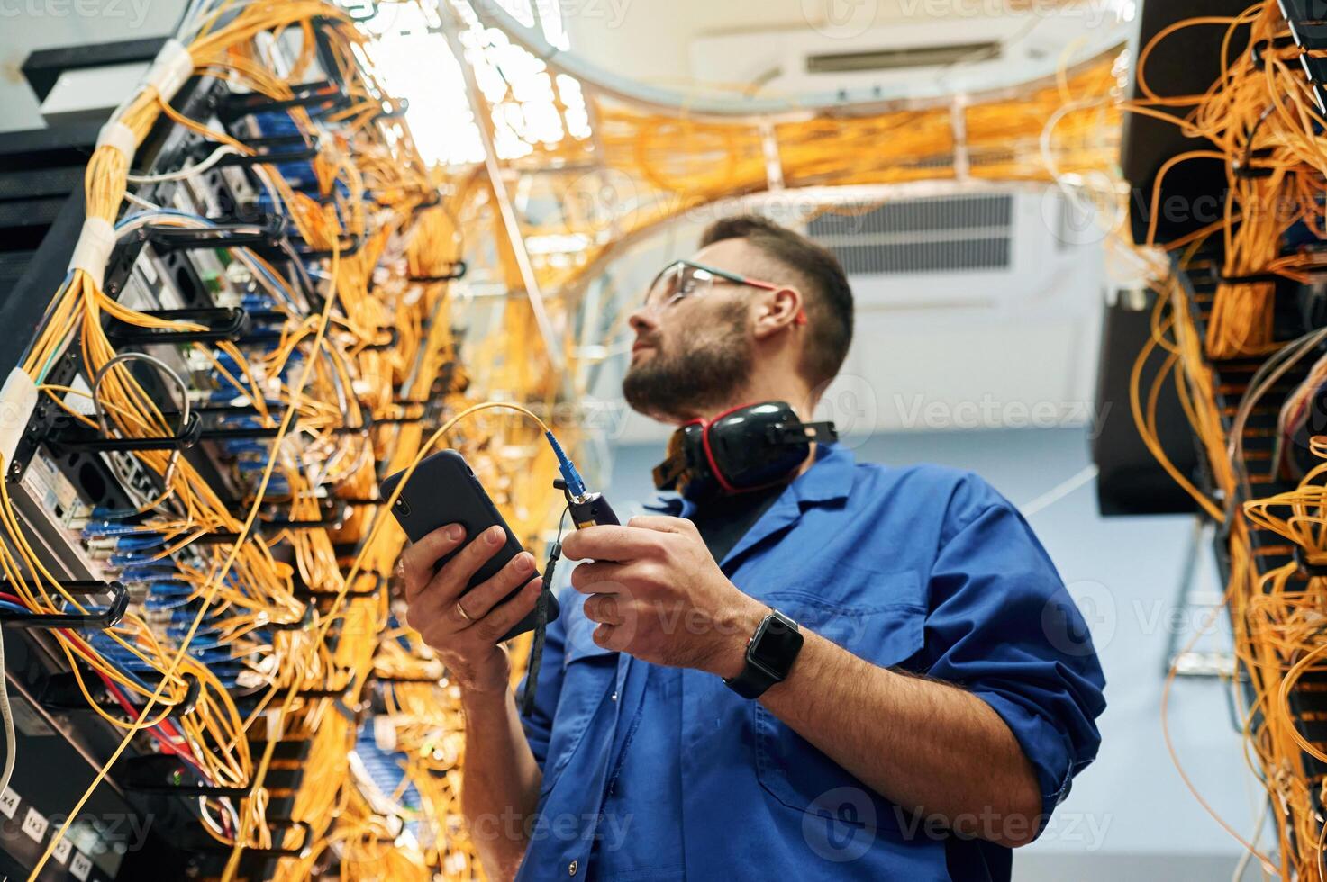 View from below.. Young man is working with internet equipment and wires in server room photo