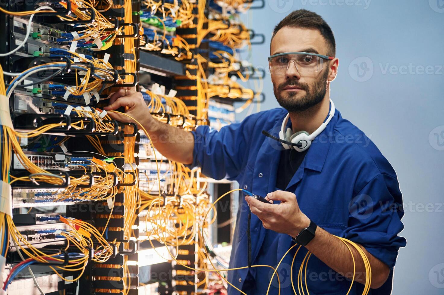 Looking to ,the camera. Young man is working with internet equipment and wires in server room photo