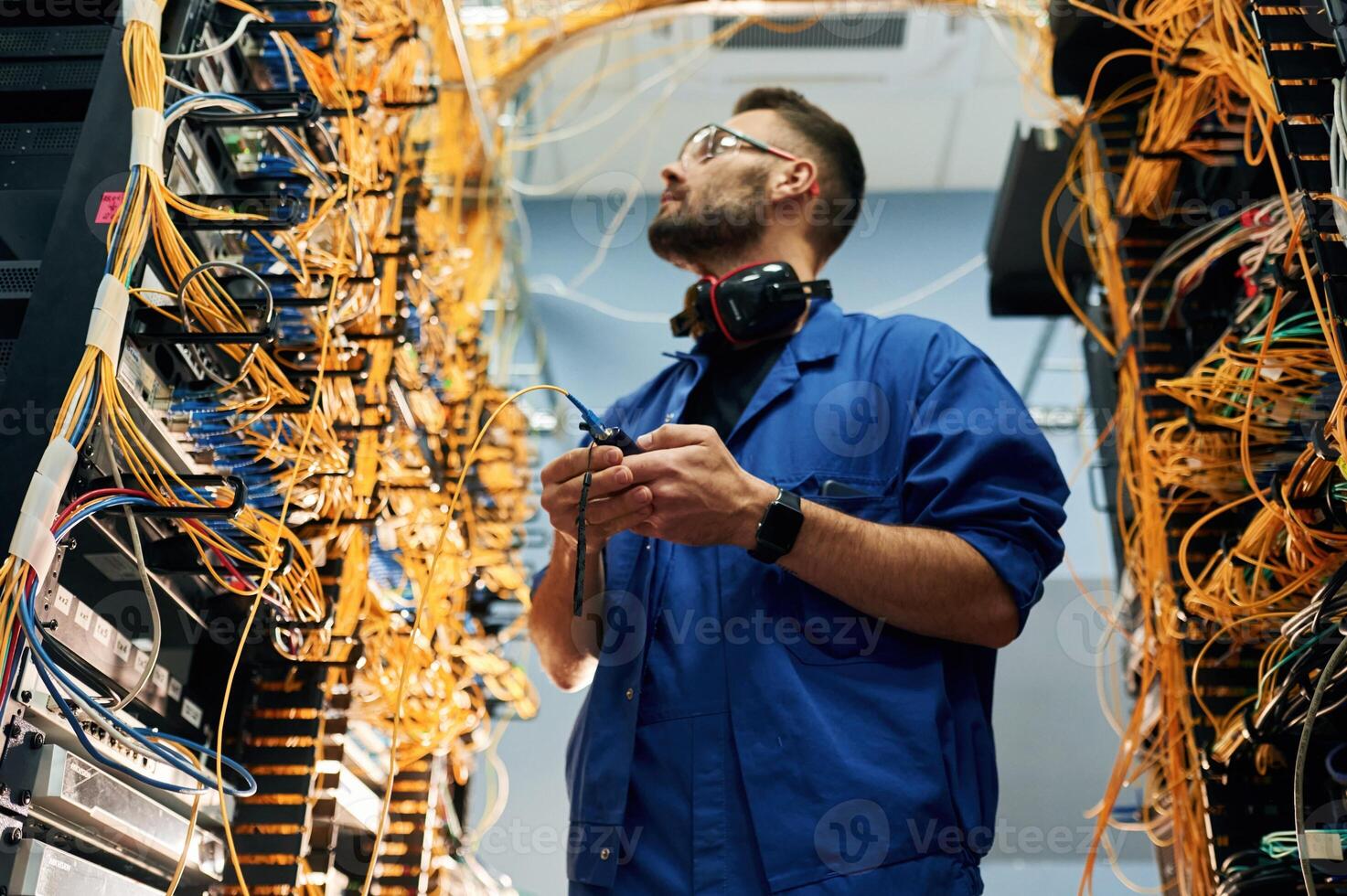 View from, below. Young man is working with internet equipment and wires in server room photo