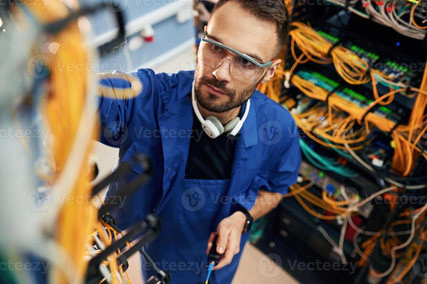 In blue, colored uniform. Young man is working with internet equipment and wires in server room photo