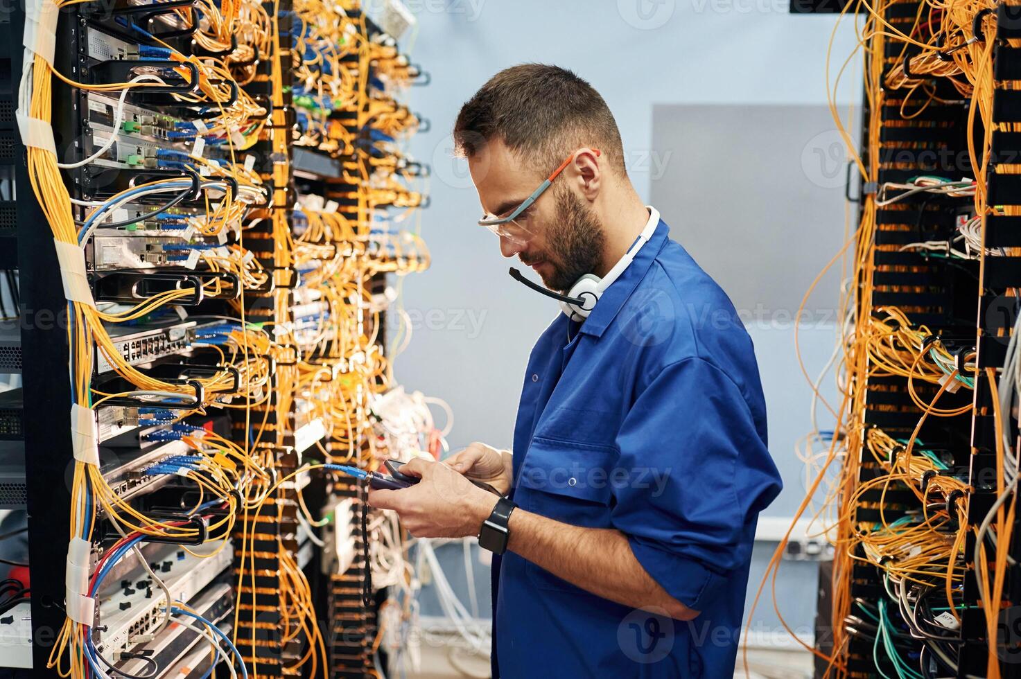 In blue colored, uniform. Young man is working with internet equipment and wires in server room photo