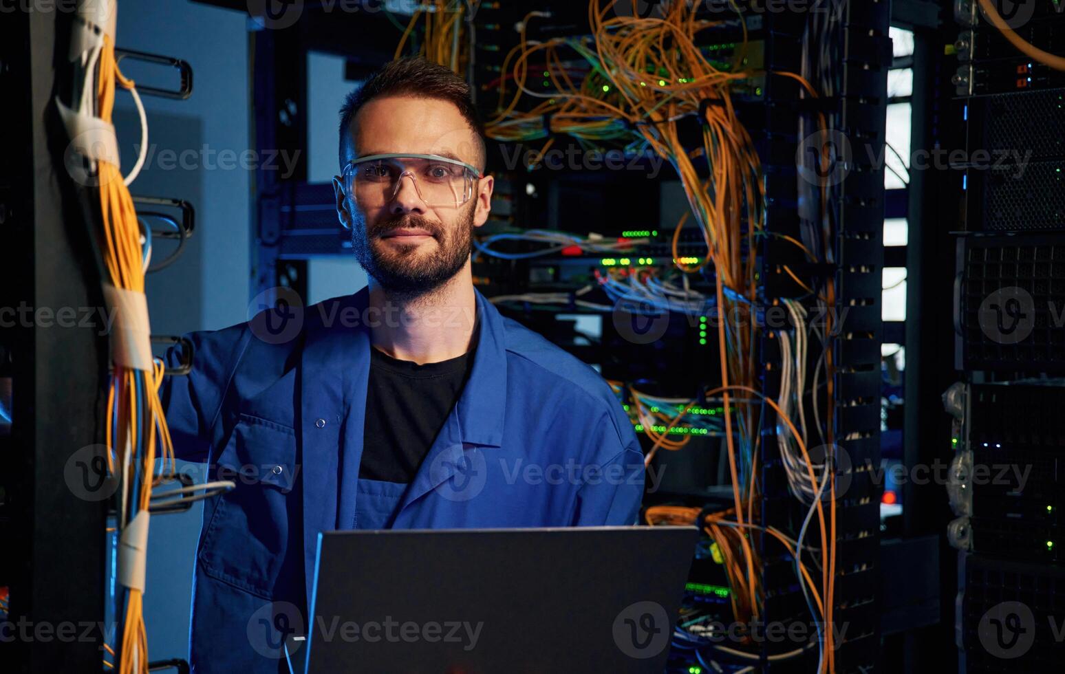 Looking, to the camera. Young man is working with internet equipment and wires in server room photo